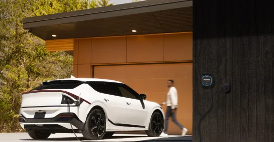 Person walking near their electric vehicle charging in the driveway